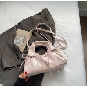 Close-up of pink glossy pleated cloud bag featuring delicate ribbon bows and metal ring handle