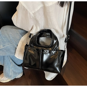 Close-up of a glossy black PU leather tote bag with dual front pockets and shoulder strap