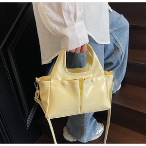 Detail of light yellow glossy tote bag with front pockets and silver hardware on stairs