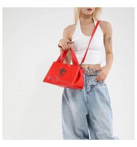 Detail of red leather tote bag with metallic cross and chain, worn by a model