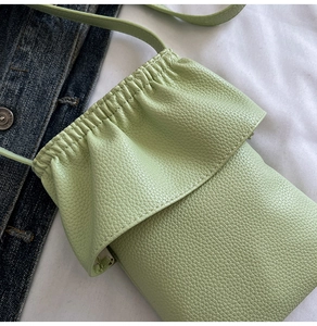 Détail du sac de téléphone en cuir grainé vert clair avec cordon sur veste en jean
