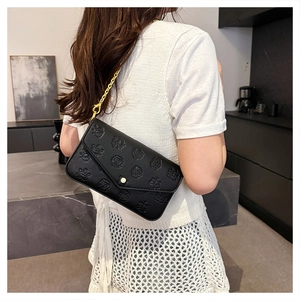 Detail of black embossed envelope bag with gold chain strap on a model shoulder