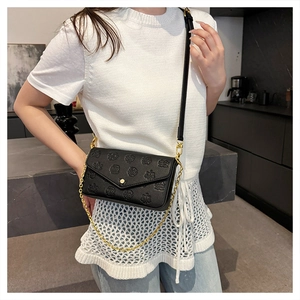 Detail of embossed rose and scale pattern on black leather crossbody bag with gold chain