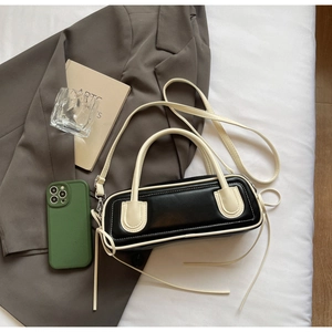 Detail of minimalist black and beige leather handbag on a bed with lifestyle props