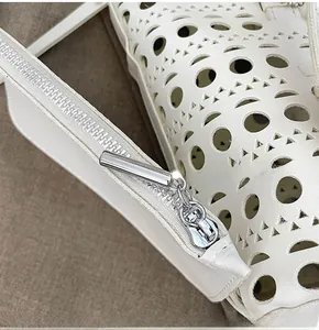 Detail of silver smooth zipper and hollowed-out leather pattern on a white tote bag