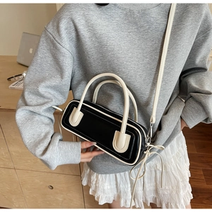 Detailed view of minimalist black and white shoulder bag worn on the arm with a gray outfit