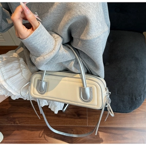 Chic beige and silver contrast baguette bag shown on a model sitting on a sofa