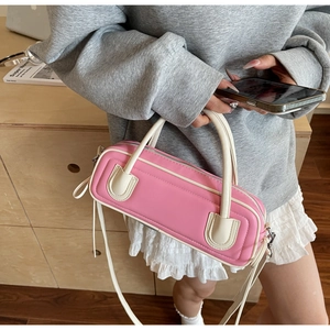 Pink baguette bag with white contrast trim and U-shaped detail worn by model in a cozy room