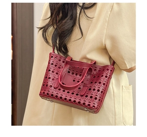Model wearing a burgundy laser-cut tote bag with intricate hollow geometric patterns