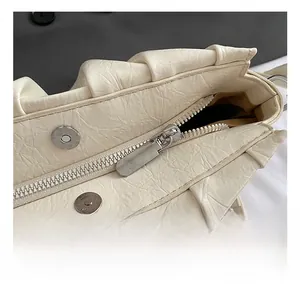 Detail view of cream pleated handbag showing silver zipper and magnetic buckle closure