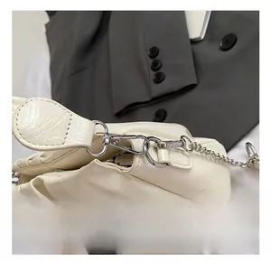 Close-up of polished silver metal hooks and chain on a pleated cream crossbody bag