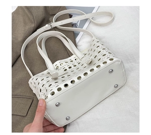 Detail view of the white hollow-out bag bottom featuring protective metal rivets and leather