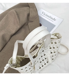 Detail of white hollowed-out tote bag with laser-cut patterns and silver hardware accents