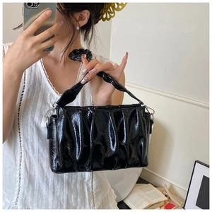 Gros plan d'un sac plissé en cuir verni noir avec poignée torsadée porté par un mannequin