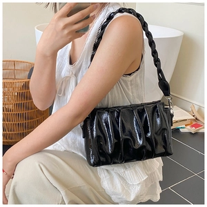 Detail of glossy black pleated underarm bag with a chunky woven shoulder strap