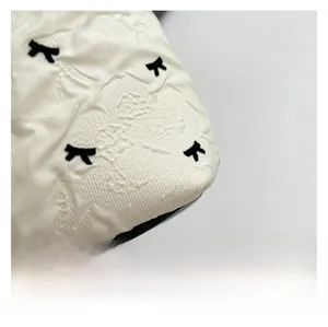 Détail du tissu blanc avec motifs floraux en relief et broderies de nœuds noirs fins