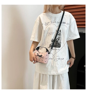 Détail du sac bandoulière rose avec nœud noir, pendentif cœur et cuir texturé gaufré