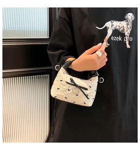 Détail d'un sac à main matelassé blanc avec broderie nœud noir et charme en cœur