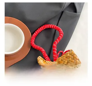 Detail of woven straw handbag featuring red and white rope handles and wooden bead closure