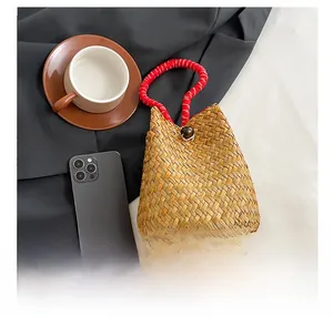 Detail showing handwoven straw handbag with red and white rope handle and wooden bead clasp