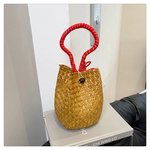 Detail of hand-woven straw bucket bag featuring a red rope handle and wooden bead closure