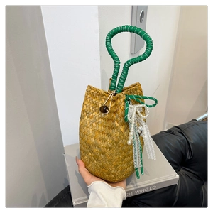 Detail view of woven straw bucket bag with green rope handle and pearl lace ornament