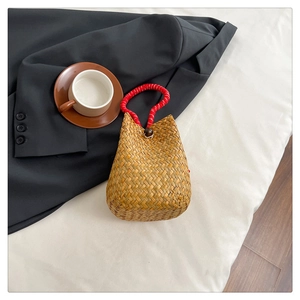 Detail of handmade straw bucket bag with red handles and wooden button on a table