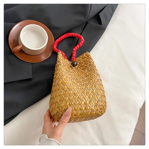 Detail of handmade straw bucket bag featuring a red and white spiral knotted handle and bead clasp