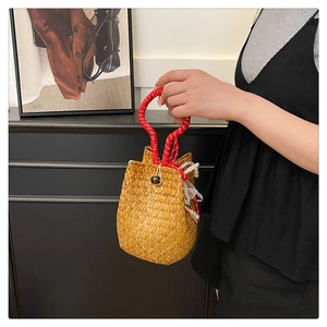 Detail of straw woven bucket bag with red handle wrap and white pearl pendant decor