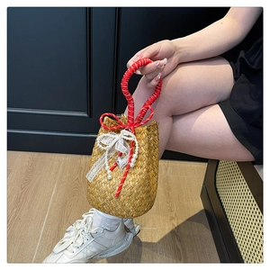 Close-up of woven straw bucket bag with red rope handle, lace bow and pearl charms