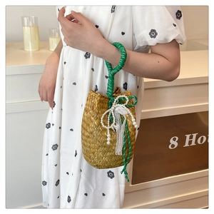 Detail of straw bucket bag with green handles, pearl bow and heart charm accents