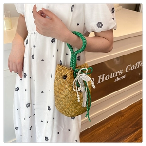 Detail of handmade straw bucket bag featuring green braided handles and pearl bow accents