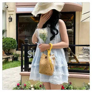 Detail of straw woven bucket bag with lace trim, pearl accents, and yellow handles
