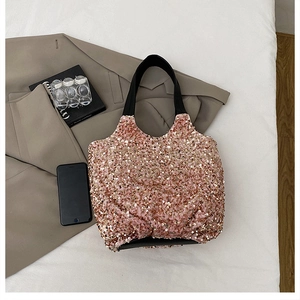 Détail d'un sac seau à paillettes or rose avec poignée en cuir sur fond de trench-coat