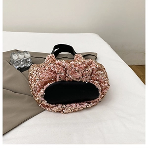 Détail d'un sac seau à paillettes roses avec anse en cuir noir posé sur un bureau blanc