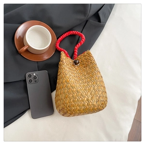 Detail of handmade straw bag featuring red woven handles and dark wooden toggle closure