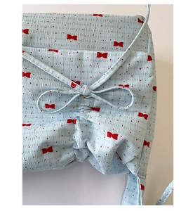 Gros plan sur un sac en tissu bleu clair avec nœuds rouges et détails de plis à cordon