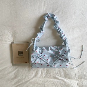 Detailed view of light blue floral fabric shoulder bag with red bows and pleated texture