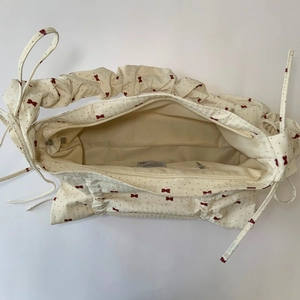 Detail view of cream tote bag with red bow print and internal zippered pocket layout