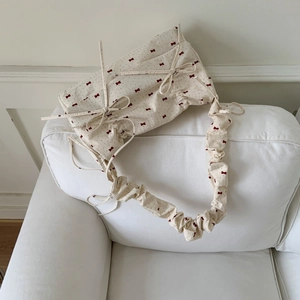 Close-up of floral fabric bag with red bow prints and ruffled strap detail on white sofa