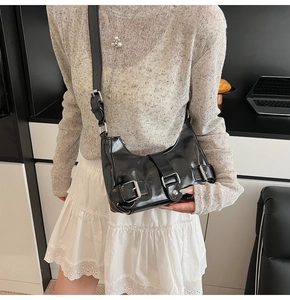 Detail view of black glossy faux leather underarm bag with three silver metal buckles