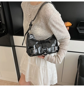 Detail of black glossy leather underarm bag with silver buckles on an adjustable shoulder strap