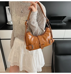 Close-up of caramel brown motor-style bag with silver buckles and adjustable strap
