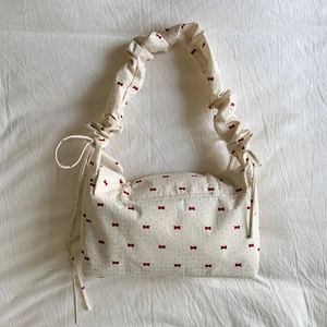 Close-up of floral fabric bag with red bow patterns and pleated shoulder strap detail