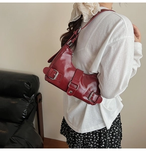 Detail of dark red biker underarm bag with glossy finish and metal buckle straps