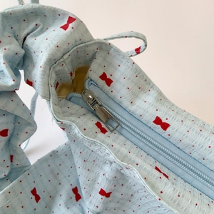 Close-up of light blue bubble texture fabric bag with red bow print and zipper