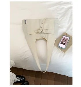 Détail d'un sac cabas en toile crème avec poches et boucle de réglage sur le côté