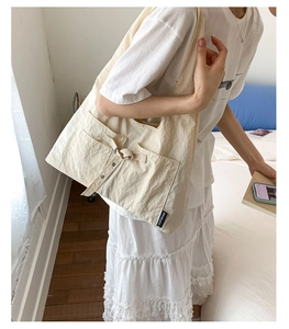 Détail du sac cabas en toile crème avec poche latérale, boucle en métal et étiquette