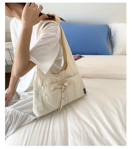 Détail du sac à bandoulière en toile blanc crème avec poche latérale et nœud décoratif