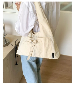 Détail du sac à bandoulière en toile beige avec boucle métallique et étiquette de marque